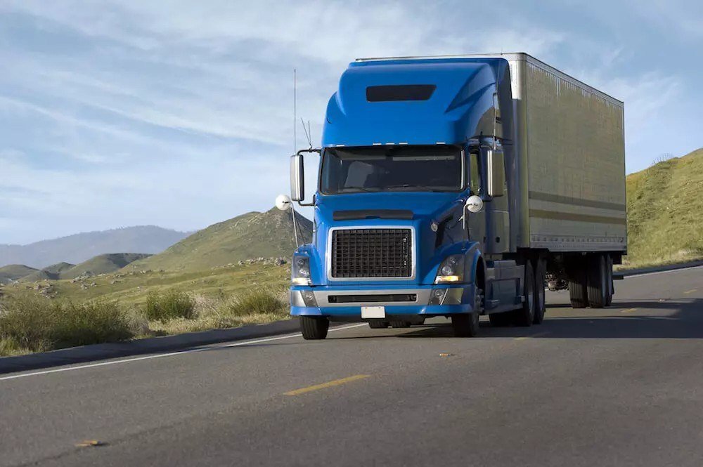 "Car Shipping New York - blue enclosed transport truck driving through hills"